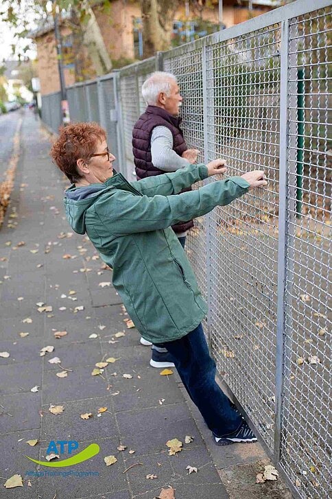 ATP-Dauerangebot Übung 9 Ältere Frau bei Ruderbewegung an einem Zaun