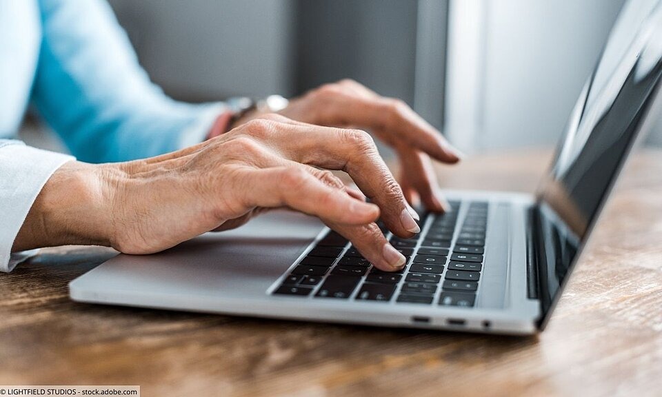 Hände einer Seniorin tippen auf Laptoptastatur