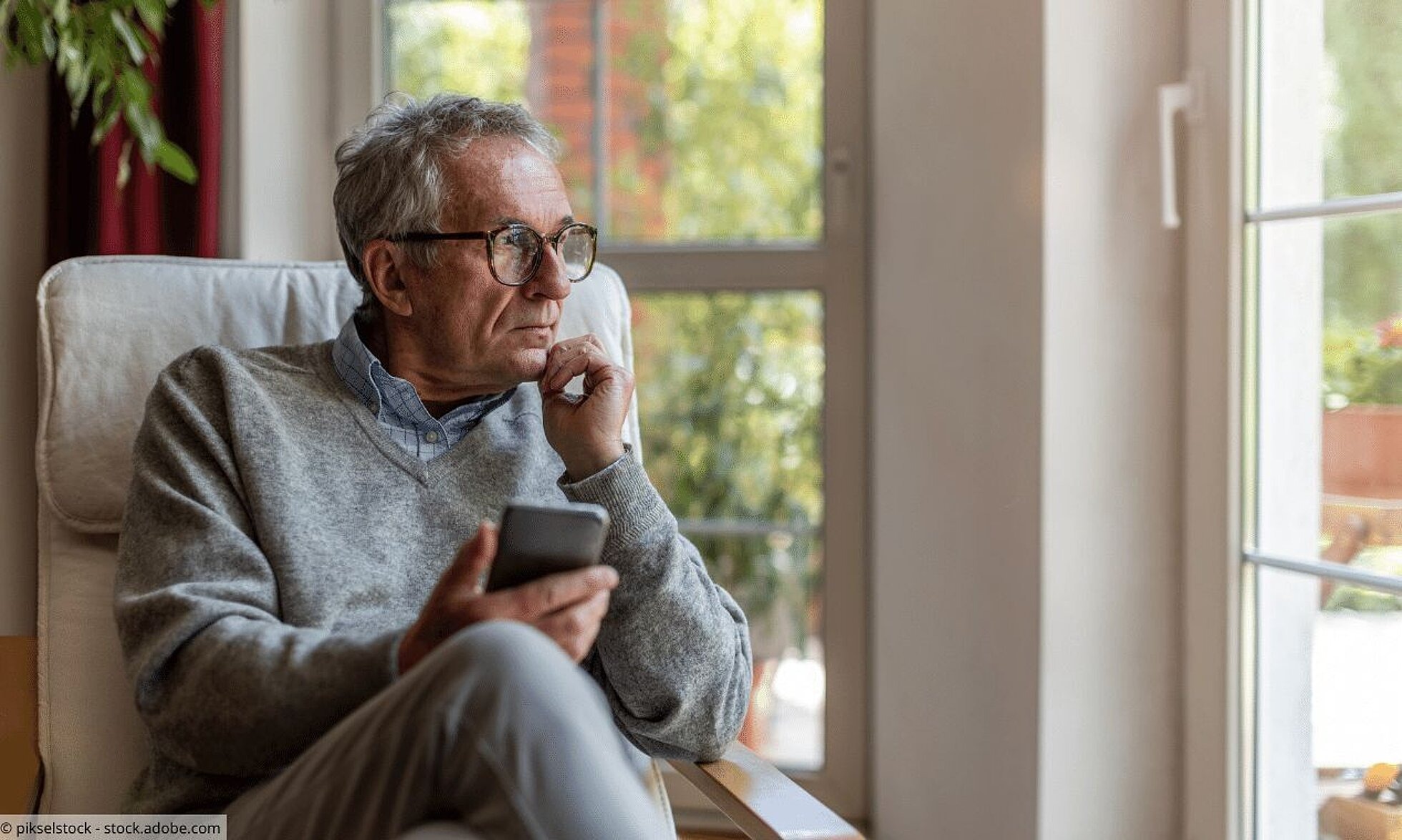 Info-Telefon Depression Älterer Mann mit Smartphone in der Hand schaut traurig aus dem Fenster