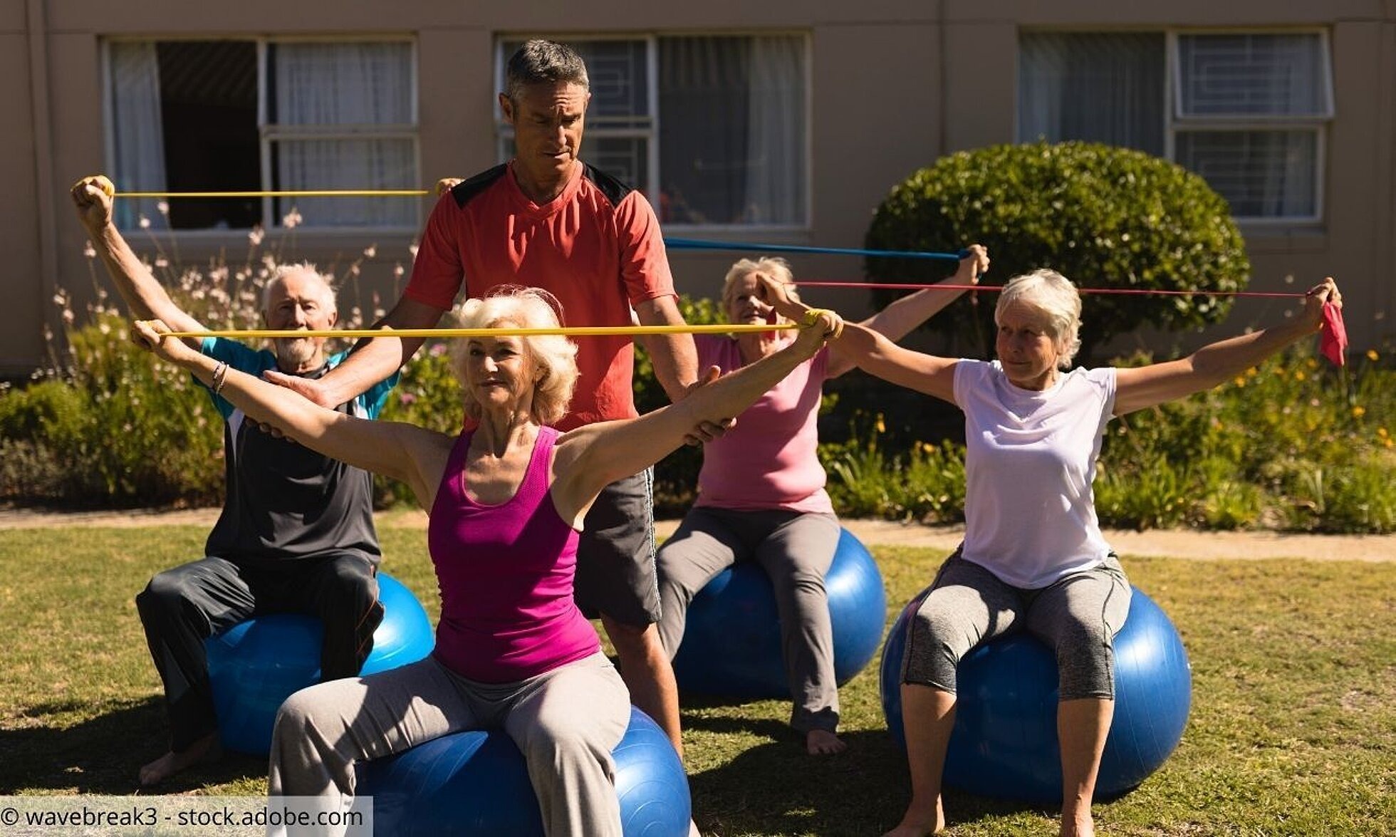 Seniorengruppe auf Gymnastikbällen mit Trainer bei Sportübungen